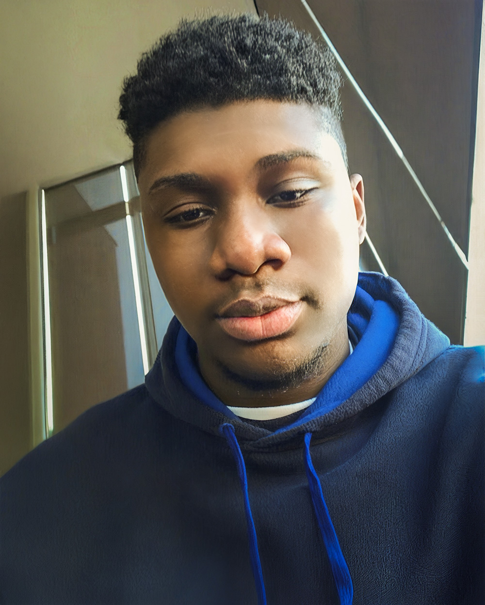 A photo of Xavier Andrews in a navy and royal blue hoodie sits near a window, looking relaxed with a soft expression.