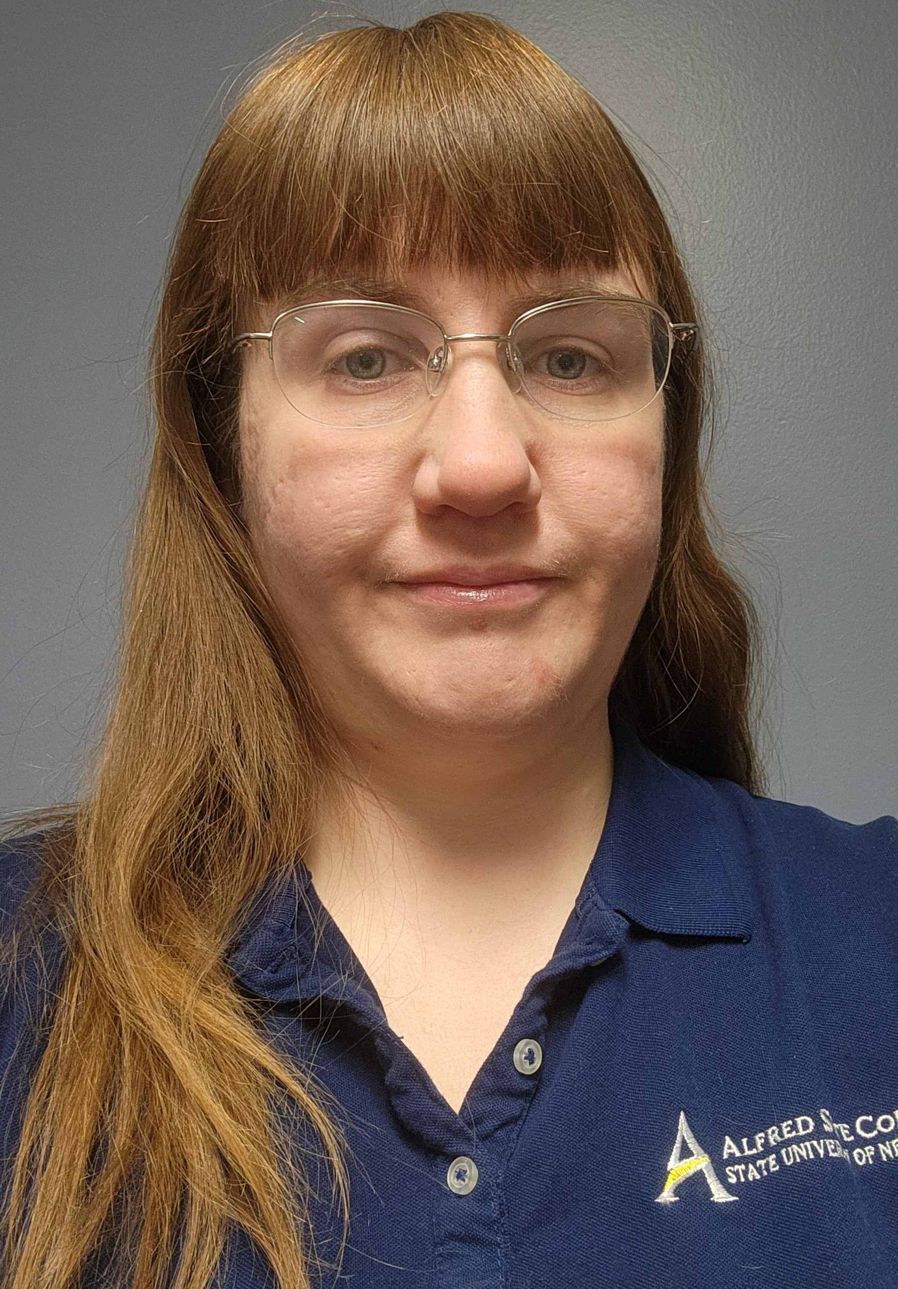 A photo of Christina Kent with long, straight hair and glasses, wearing a navy blue polo shirt, against a simple gray background.