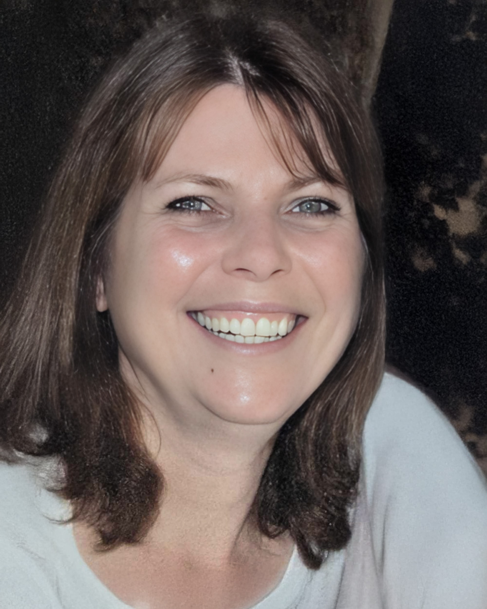 A headshot of Colleen Dolph with shoulder-length brown hair and bright eyes, wearing a light-colored top.
