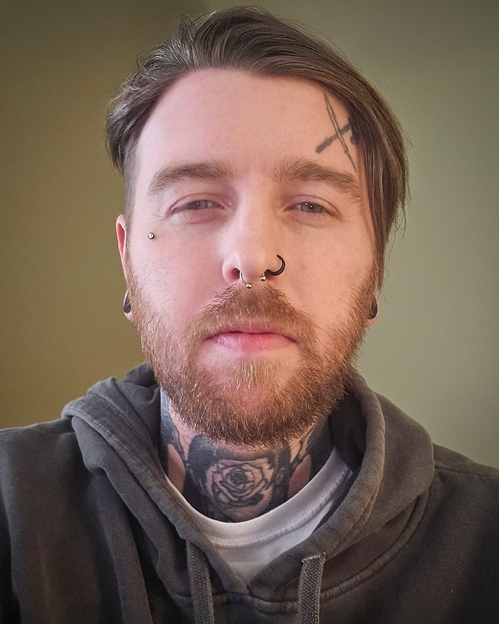 A headshot of Nicholas Eason with short hair, a beard, and multiple facial piercings.