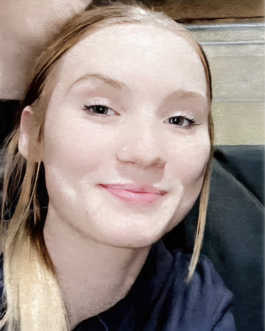 A headshot of Ashlyn Hoffman with light hair pulled back and a warm, subtle smile poses in soft lighting. She is wearing a dark shirt, set against a neutral indoor background.