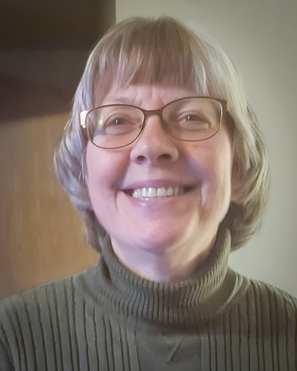 A headshot of Marilyn Robin with short, light gray hair and glasses, smiling warmly at the camera. They are wearing a ribbed olive-green turtleneck sweater, and the background features soft, neutral tones.