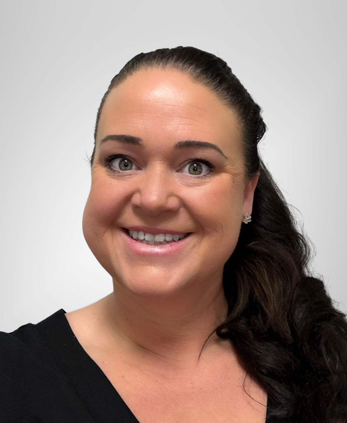 A professional headshot of Lynn Brennan White with long dark hair pulled back, wearing a black top and small stud earrings. She is smiling and set against a plain, light-colored background.