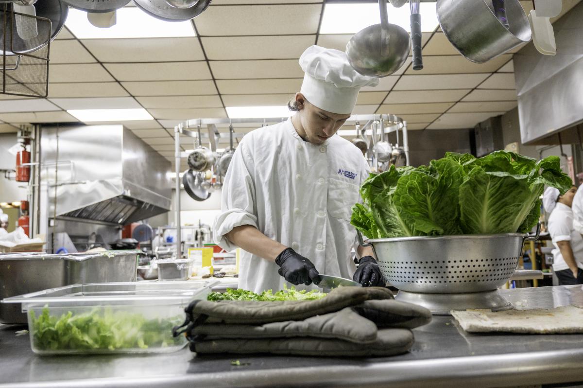 A student in a kitchen chopping vegetables