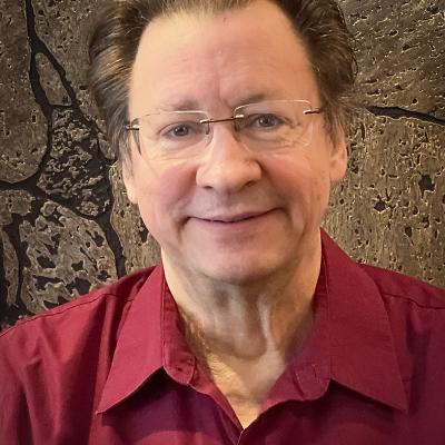 A headsot of Leroy Hanchett with neatly combed hair and glasses, wearing a burgundy button-up shirt.